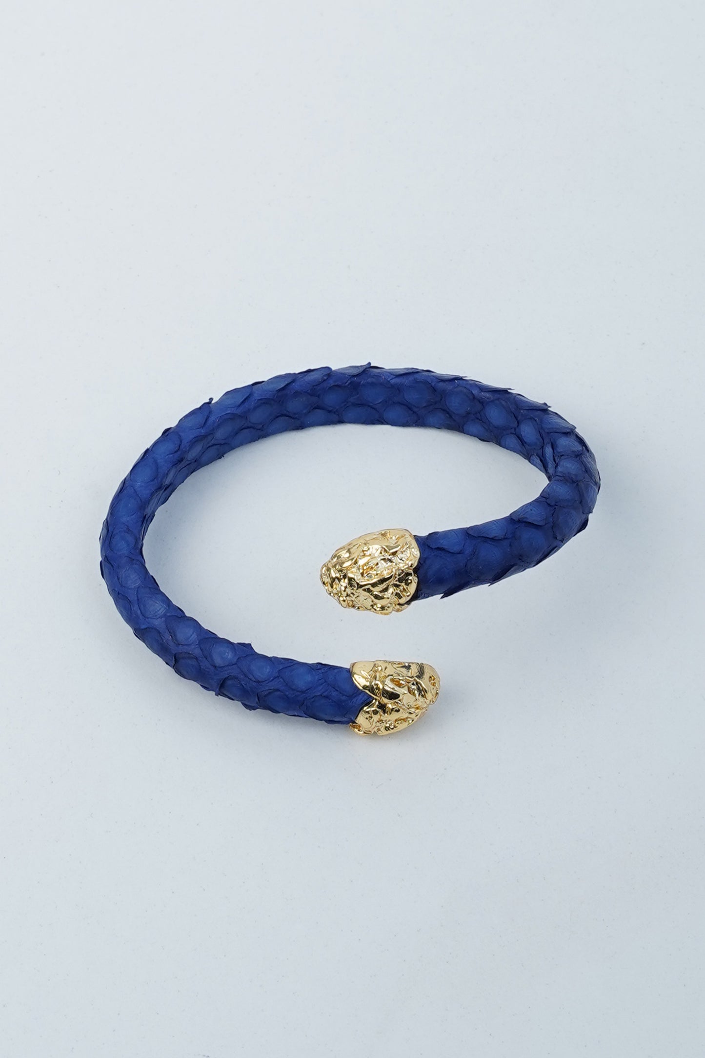 Sky blue python-texture leather bracelet with gold-plated engraved ends, displayed flat and worn by a model