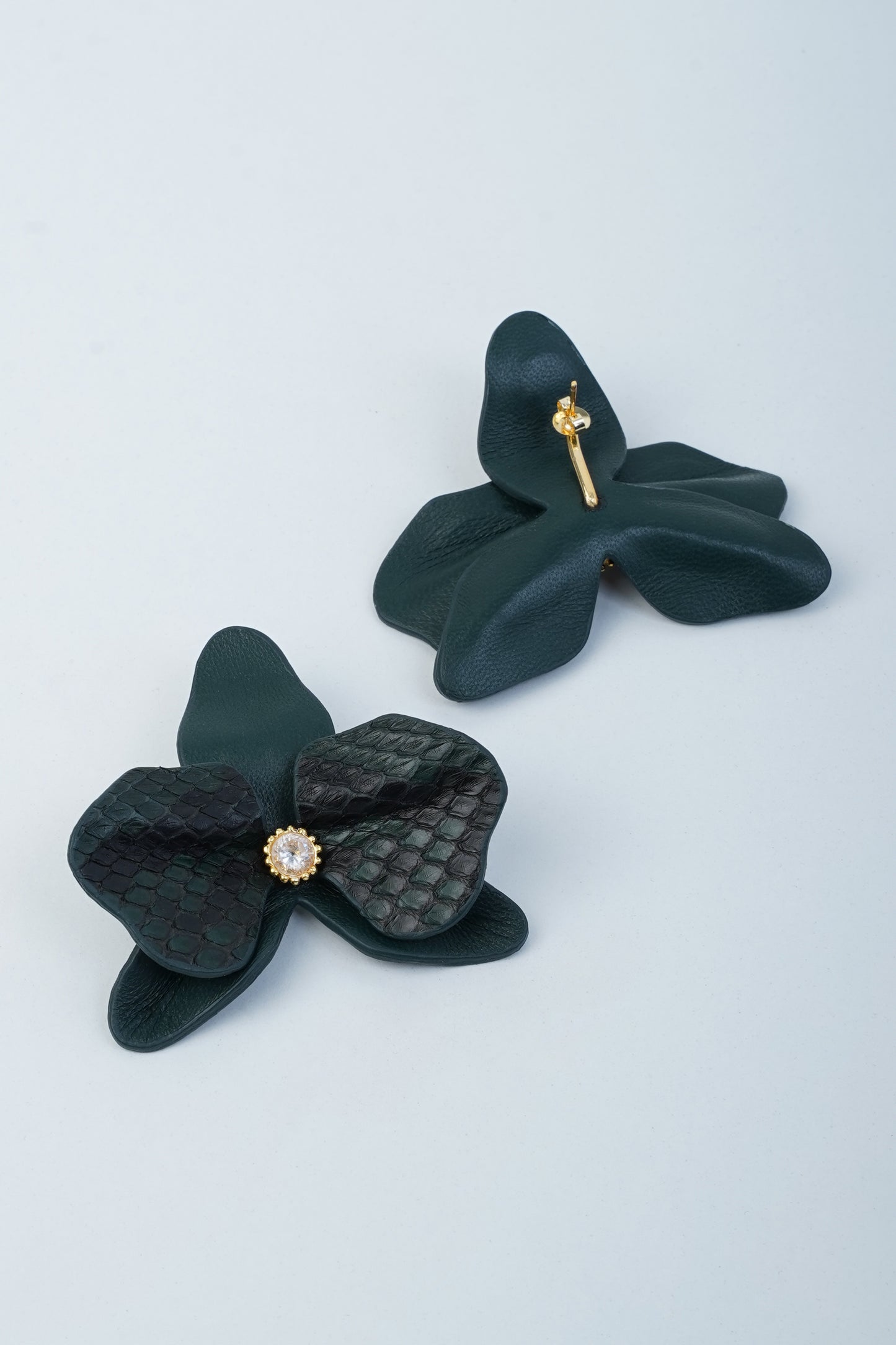 Black orchid-shaped leather earrings with gold and stone accents on light background.